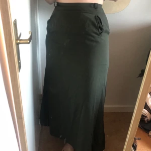 Vintage kjol lång - Mörkgrön kjol köpt second hand, går ner till fotvristen typ. Svår att fånga på bild men väldigt fin irl, bra skick. Fickor på framsidan, dragkedja och knapp på baksidan. Tjockt tyg, har ett extra innerlager för värme, perfekt för höstväder! 