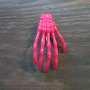 Rosa skeletthand hårspänne - Chockrosa hårspänne i plast som föreställer en skeletthand. Inköpt på konvent. Frakt tillkommer. 