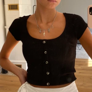 T-shirt med knappar - Jag säljer denna svarta urringade T-shirten med knappar framtill från ginatricot. Den är endast använd ett fåtal gånger och är i fint skick. Tror den är köpt för 199kr men jag säljer den för 80kr+frakt. Först i kvarn. Skriv vid intresse☺️⚡️