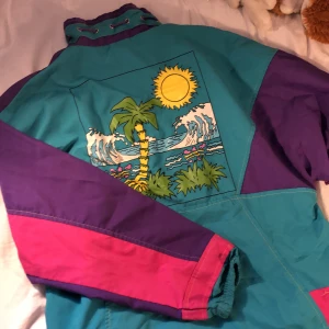 Vind jacka i färgglada färger :) - En jätte skön vindjacka med 80-tals motiv på ryggen :) Den är i nyskick och enbart använt ett fåtal gånger. Man kan spänna in längst ner på jackan så vilken storlek som helst kan ha den, även jag som har s/xs :)Står ingen storlek men skulle säga L :) Köparen står för frakten <3