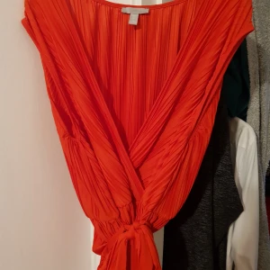 Röd plisserad omlottopp HM L XL - Fin röd plisserad omlottkjol med knytband från HM i stl L men stor mer som XL. Fint beg skick. Djur finns i hemmet 