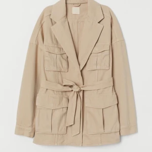 Ljusbeige jacka med skärp  - En jättefin ljusbeige jacka i relik från HM. Använd fåtal gånger. Går att ha skärp knäppt i midjan eller utan. Storlek 42. Passar både större och mindre beroende på vilken passform man vill ha! 