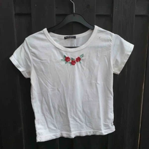  - Vit tröja från Brandy Melville med broderade röda rosor på. Hyfsat kort och tight i passform.  Du står för frakt