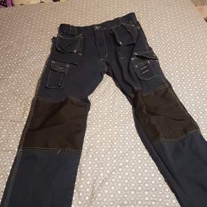 Det är ett par snickarbyxor med ganska många fickor dem är mörkblå och svarta, dem är gjorts i jeans.