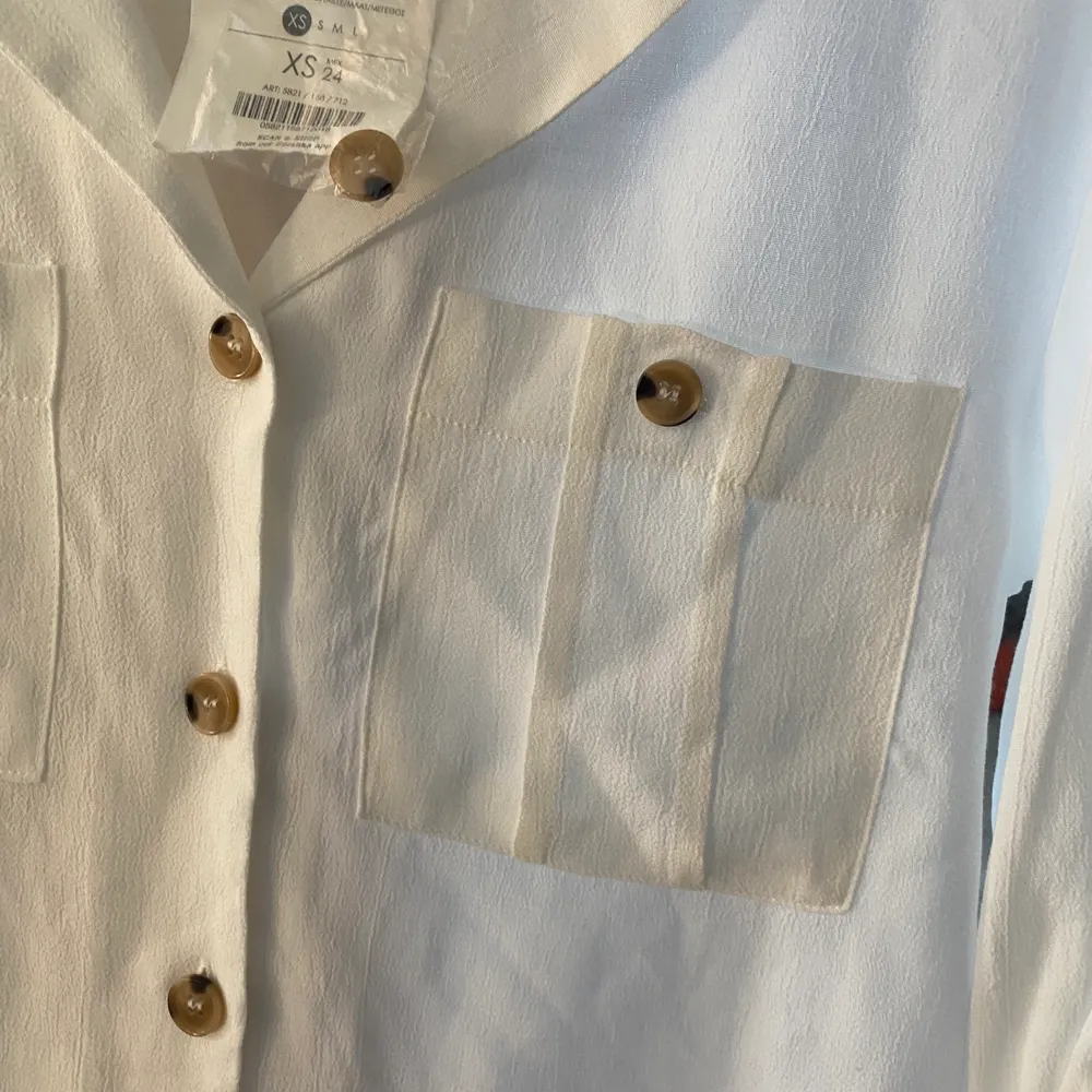 Superfin vit skjorta som har fina ”bruna” knappar på. Aldrig använd då prislappen är kvar och du får med en extra knapp. Armarna kan man både ha som det är på bilden eller knäppa upp och ha som en vanlig ärm. (priset är diskutebart). Skjortor.