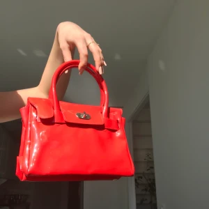 Röd liten lackväska  - Sjukt fin lackväska i rött! Helt perfekt skick förutom några små prickar på baksidan (tror dock de går bort med lite papper och spray) Perfekt size tycker jag!  Tillkommer tillhörande axelband också. Möts på söder annars står köpare för frakt, 42kr🌼💕