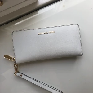 Michael kors plånbok i nyskick  - Jätte fin Michael kors plånbok i vit/guld. Köpt på NK i Stockholm så självklart är den äkta. Använd nån gång så Inga defekter alls, ser ut som ny. 60kr Frakt tillkommer.