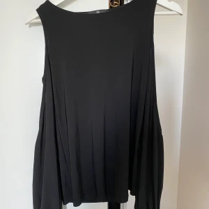 Blus med öppna axlar Missguided - Svart blus från Missguided med öppna axlar och knytbara snören i armarna. Använd en gång. Strl 36, passar XS/S. Kan mötas upp i Västerås annars står köparen för frakt. 
