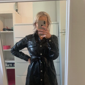 Lång fake-läderskjorta från NAKD - Lång, svart skjorta i ett mjukt och tunt läder-liknande material från NAKD. Kan användas som en klänning på mig som är ca 163. Endast testad, nyskick. 