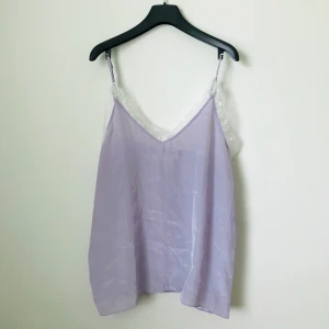 Ljuslila linne med spets - Jättefint ljusviolett linne i silkesliknande material med spetsdetalj. Från koreanska märket STYLENANDA. Köpt för 300 kr men aldrig använt 💕