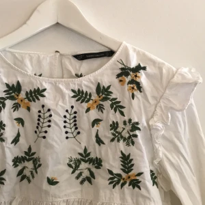 Blus  - Lätt utställd blus, tight över bysten som har söta broderier i grönt och gult! Volang vid armslut! Använd fåtal gånger! Frakt ingår! 🍀