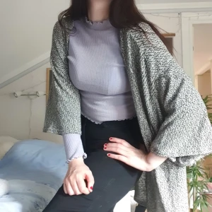 lång grå kofta - når ungefär till knävecken. är spräckligt grå med 3/4-ärm. 