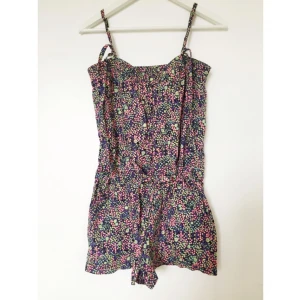  - Jumpsuit med fickor, knappar fram och snörning i midjan samt snören till axelband. Småblommig och fräsch. 