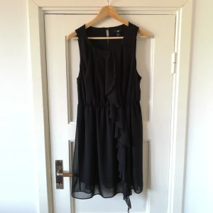  - Svart klänning med detaljer i volang. 