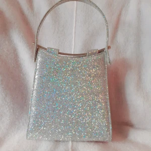 Glittrig väska - Glitterväska från Spanien! Går att använda både som handväska och crossbody-då det finns en silverkedja på insidan att använda som axelrem. Används för sällan av mig så därav säljer jag den vidare!🌍💌