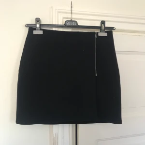 Scary kort kjol - Svart kort, Penn/omlott kjol från Monki. Förslutes med dragkedja och knapp på insidan. Tjockt tyg så passar även bra på hösten med strumpbyxor. Strl S. 
