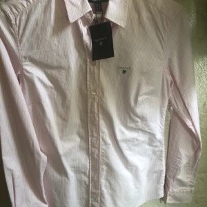 GANT skjorta oanvänd - Helt ny skjorta från GANT. Rosa/vit randig i slimfitmodell. Aldrig använd, prislapp kvar. Köparen står för frakten. Fraktar endast. Nypris: 999kr