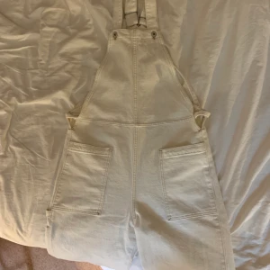 Hängselbyxor från Levi’s - Ett par vita hängselbyxor från Levi’s i rak modell. De knyts baktill vilket gör att de ger en mer figurnära passform i midjan. Motsvarar ungefär storlek S. I jättebra skick bortsett från att de slitits nedtill pga att jag är kort:/. Frakt tillkommer.