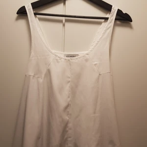  - Vitt linne med lagom breda band, figursydd runt bysten men lös och en vågig skurning i botten. Urringad. 