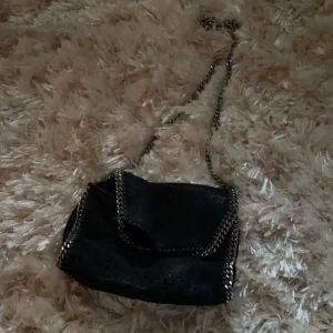 Stella McCartny väska   - Säljer min Äkta Stella väska som jag köpte för ungefär 2 år sen. Den är använd men i bra skick. Enda felet är ett litet hål under väskan men det syns knappt. På bilden är väskan lite knuten vid bandet för jag föredrar den kortare men man kan ha den lång också. Köpte den på rea så säljer den därför för bra pris. Modellen är: SVART, falabella shoulder bag