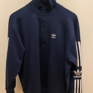 Adidas half zip hoodie - En adidas half zip hoodie i marinblå, endast använd en gång, säljer pga att den inte kommer till användning orginal pris 400, säljer för 200