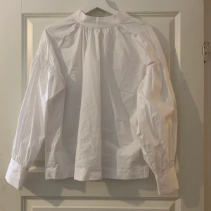 Vit blus i skjormaterial - Vit blus i skjortmaterial, med lite högre krage och ballongärmar från H&M. Aldrig använd. Strlk S. Skriv för mer info/bilder. Pris kan diskuteras.
