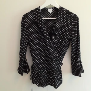 Prickig blus  - En svart blus med vita prickar. Volang i ärmar, mitt på och längst ner på tröjan. Man knyter den omlott på sidan. Frakt ingår i priset💋