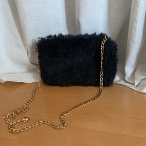Fluffig svart handväska  - Säljer en liten fluffig handväska med guldig kedja. Passar perfekt för utekvällar eller om man bara vill piffa upp en outfit. Axelbandet går att ta av om man klipper upp kejdan och då kan man bara ersätta med något annat om man vill det. Frakt ingår💜