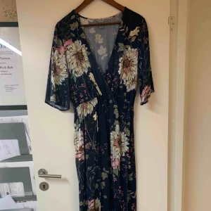  - Långklänning med blommigt mönster. Knapp framtill vid urringningen. Använd en gång. 