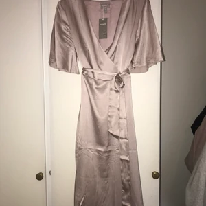 Sidenklänning - Beige/rosa-klänning i siden från H&M premium quality. Jag köpte den för 1499kr och har aldrig använt den. :) Klänningen är i storlek 40 men passar de flesta då modellen är omlott och man knyter och anpassar den efter midjan.