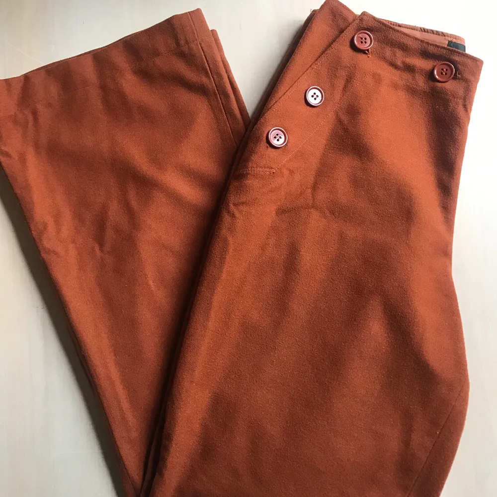 Några raka bruna kostymbyxor i brunt. Öppnas och stängs med knapparna på framsidan. . Jeans & Byxor.