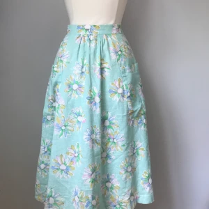 50-tals blommig kjol - Färgglad lång vid kjol i pastellfärger med blommönster. Det sitter två rymliga fickor fram och en dragkjedja bak. Kjolen har även ett innertyg. Plagget är i mycket gott skick och jag har aldrig använt det. Storleken är runt 38.