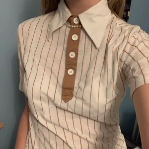 Topp 70-tal - Vit topp med bruna ränder och knappar. 70-talsstil (kolla kragen🤩)!! Köpt på vintagebutik för några år sedan. Nött skick men fortfarande hel och fin, älskad! ♥️