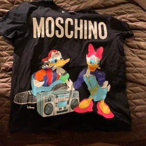 Moschino T-shirt - Jätte fin minutes edition t-shirt från H&M och Moschinos samarbete! Använd en gång och är i jätte fint skick. Inga spricknibgar. Kontakta mig vid intresse och buda i kommentarerna eller kontakta mig