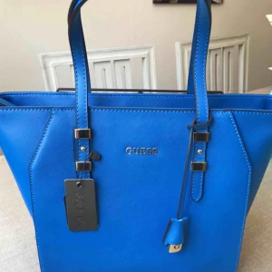  - BUD PÅ TRADERA! Helt oanvänd, tags kvar! Köpt för 120 €~ 1250kr  Väskan är en äkta Guess small tote väska ”Sissi” som jag köpte i deras butik i Torrevieja. En blå riktigt snygg handväska som får plats med en laptop eller liknande.