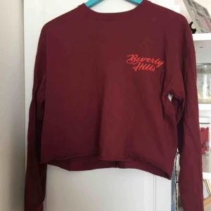  - En tröja köpt på carlings. Vinröd med text ”Beverly Hills” på vänstra sidan.