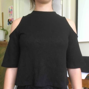 - Svart ribbad top m trekvarts och vid ärm. Cold shoulder. Fint skick.