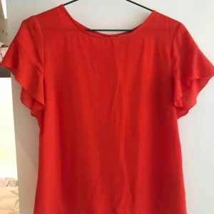  - Röd/orange topp med volang på ärmarna. 
