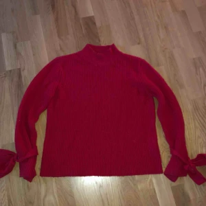  - En röd stickadtröja köpt förra sommaren. Knappt använd. Fina knyt detaljer vid ärmarna. Köpare står för frakt :-)