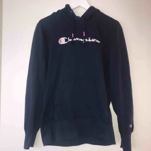  - Marinblå hoodie från Champion i tunnare material med broderade detaljer (på luvan och frampå) i vitt och rosa. Liten i storleken! Köpt från Junkyard för ett år sedan för cirka 700 kr och är max använd 3 gånger. Säljs för 350 kr och i priset ingår frakt.