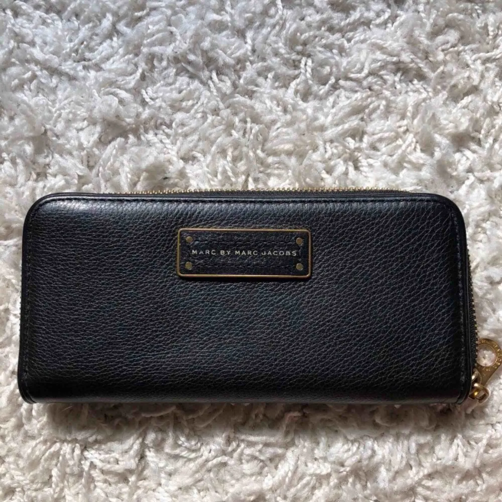 Säljer denna plånbok från Marc Jacobs, köpt på NK. Plånboken är knappt används, alltså i väldigt fint skick! Svart med gulddetaljer. Accessoarer.