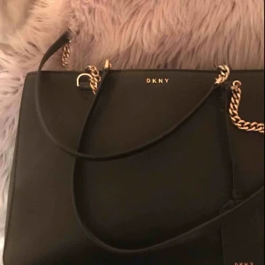  - DKNY väska i matt. Snål använd. Nypriset på denna modell ligger på 3000kr. Fodral följer med. Skickar bilder på olika delar av väskan vid intresse. Kan gå ner i pris vid snabbköp. Dubbla handtag,Innerfickor med dragkedja, Dubbla fack, Mått 36x24x11cm.