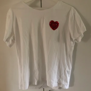 Söt t-shirt med paljett hjärta  - En söt vid t-shirt med ett paljett hjärta. Simpel med gullig och enkel. Använd fåtal gånger. Storlek M men passar både mindre och större storlekar skulle jag säga. Köparen står för frakten.