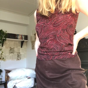 Glittrig topp - Festligt glittrigt linne med rödbrunt mönster och guldiga glitterdetaljer. Storlek 38-40 och i mycket gott skick!