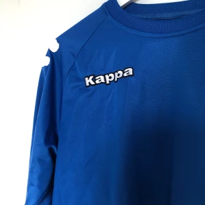 Kornblå Kappatröja  - En kornblå kappatröja, skicket på märkena är lite slitet (se bild). SAMFRAKTAR