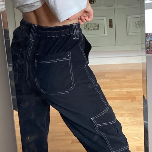 Trendiga cargo byxor från Urban Outfitters  - Svarta byxor med vita sömmar från Urban outfitters i storlek w27. Köparen står för frakten.