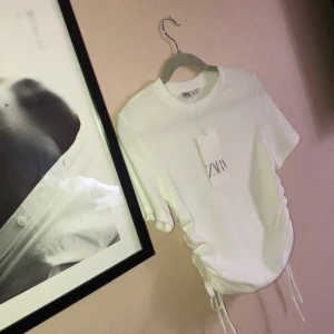 tshirt med snörning  - Oanvänd vit t-shirt från Zara med snörningar på båda sidor. Super fin men kommer ej till användning. Storlek M men skulle säga passar en S oxå.