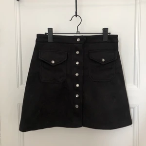 Svart mockakjol - Fin mockakjol i svart med knappar. Knappen på ena fickan har lossnat under så den går inte att knäppa, dock inget som syns. Köpt second hand, står stl 2 inuti. Skulle uppskatta att den motsvarar 36/S. Fint begagnat skick