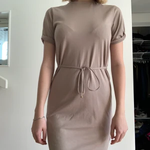Filippa K Crew Neck T-Shirt Dress - Superfin gråbeige klänning från Filippa K som tyvärr inte kommer till användning längre. Köptes förra sommaren på Åhléns för 1100kr nypris. Runt midjan har den ett band med guldiga pärlor i slutet. Klänningen har en normal passform. Jag är 165 cm lång och är ganska normalt byggd, brukar vanligtvis ha S men i denna har jag XS.