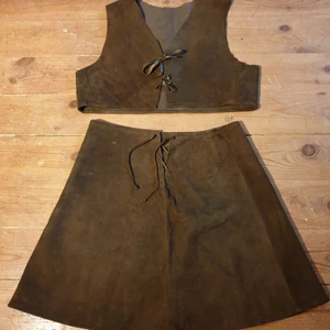 Mockaväst & kjol - Mockaset, väst och kjol.  Mått mätt rakt över  Kjol:  Midja 39 cm Längd 46.5 cm Väst: Längd 37cm Armhåla till armhåla 48 cm  110:- plus frakt 63:- spårbart 